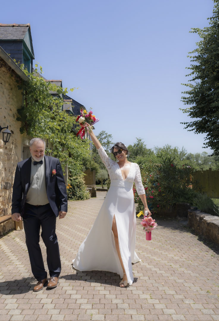 Photo lumineuse de la mariée brandissant spontanément son bouquet et faisant virevoleter sa robe de mariée lors du départ vers la cérémonie de mariage au domaine de la Métairie à Ossun, Hautes Pyrénées