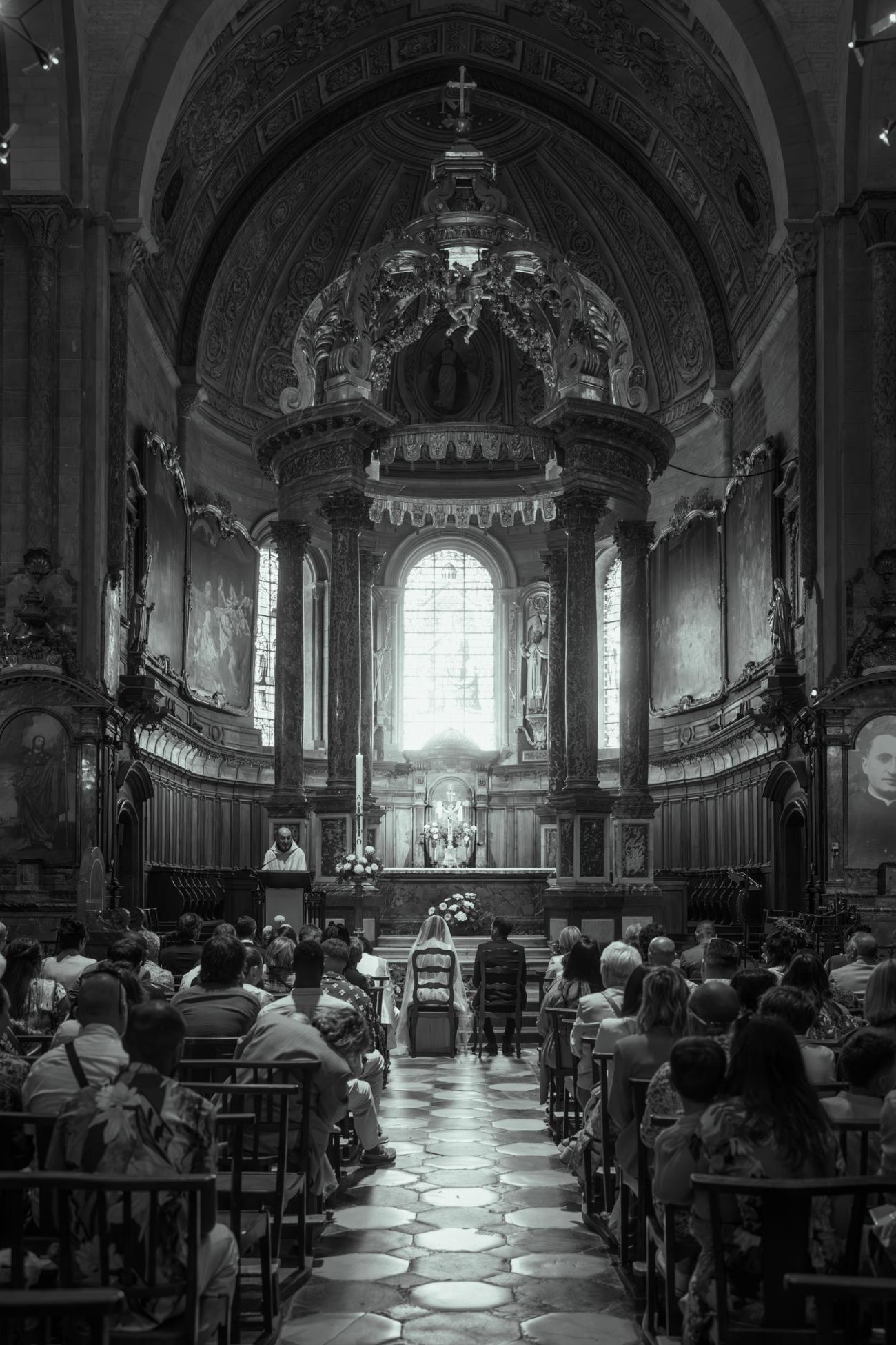 Cérémonie de mariage en noir et blanc à la cathédrale de Tarbes : les mariés face à l'autel et au grand baldaquin.